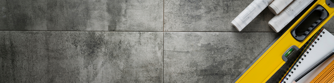 Construction tools including a level, tape measure, and blueprints on a concrete floor.