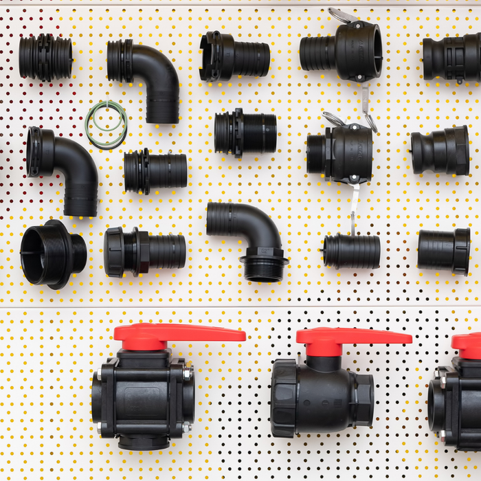 Collection of black plumbing pipes and fittings on a white pegboard with yellow dots.